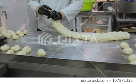 The chef is preparing the dough, the cook is working with the dough in the kitchen, the chefs are sculpting the dough for the bakery. The chef is preparing the dough, the cook is working with the dough in the kitchen, the chefs are sculpting the dough for the bakery. 107871323