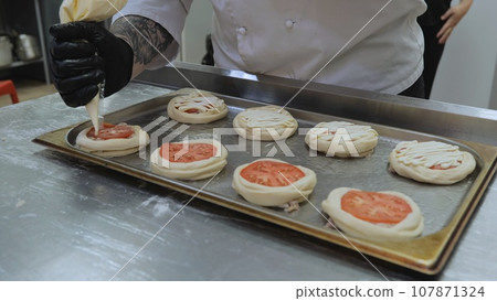 The baker prepares pastries with minced meat and tomato, the cook prepares pastries in the kitchen, the hands of the cook prepare pastries close-up. The baker prepares pastries with minced meat and tomato, the cook prepares pastries in the kitchen, the hands of the cook prepare pastries close-up. 107871324