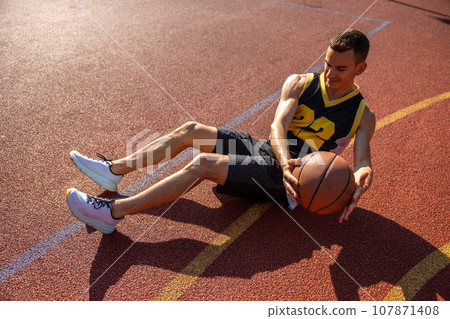 Sporty man doing abs workout with ball outdoor on basketball court. Sporty man doing abs workout with ball outdoor on basketball court. 107871408
