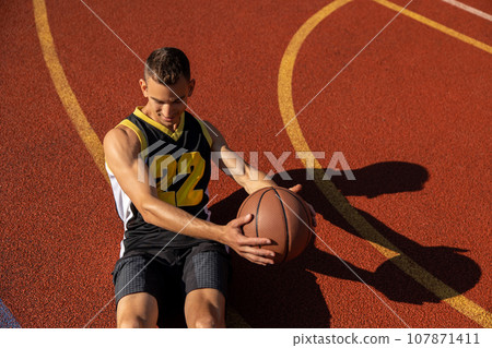 Athletic man doing sit ups and crunches exercising abdominal muscles outdoor on basketball court. 107871411