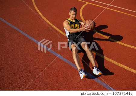 Athletic man doing sit ups and crunches exercising abdominal muscles outdoor on basketball court. 107871412