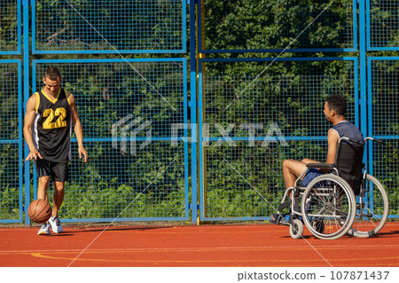 Man with disability in wheelchair and personal trainer for recovery motivation playing basketball. Man with disability in wheelchair and personal trainer for recovery motivation playing basketball. 107871437