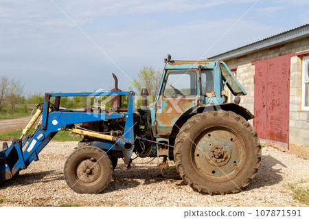 Tractor on the farm. Farmer's equipment. Blue tractor against the background of the village. Tractor on the farm. Farmer's equipment. Blue tractor against the background of the village. 107871591
