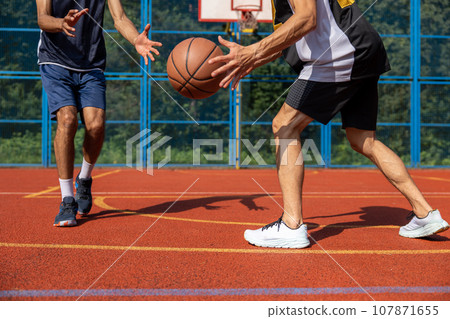 Two unrecognizable men playing basketball in court outdoors. 107871655