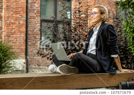 Pretty young woman in eyeglasses working on laptop outside Pretty young woman in eyeglasses working on laptop outside 107871679