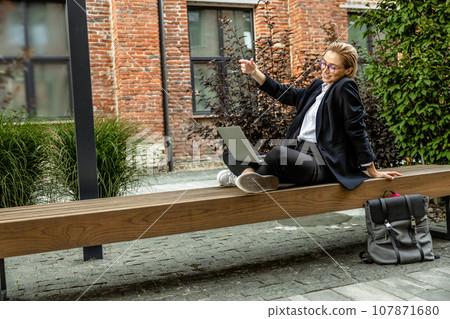 Pretty young woman in eyeglasses working on laptop outside Pretty young woman in eyeglasses working on laptop outside 107871680