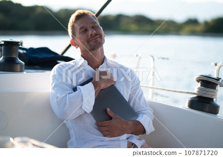 Man on a yacht deck with alaptop in hands Man on a yacht deck with alaptop in hands 107871720