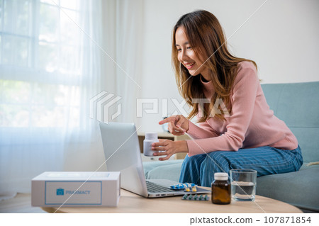 Telemedicine. Young woman sick holding drug video call online consultation ask doctor consulting about illness and medication on laptop computer at home, Method of taking pill, medical online support 107871854