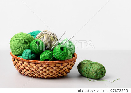 Green knitting balls in a basket with knitting needles on gray background. Set for the hobby of knitting warm clothes or toys. Concept needlework 107872253