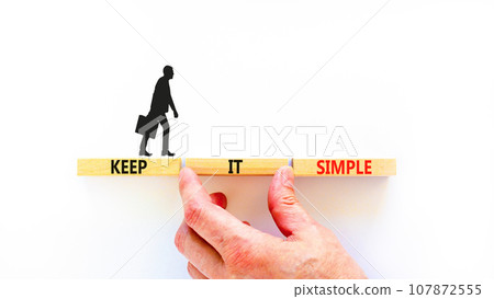 Keep it simple symbol. Concept word Keep it simple on beautiful wooden block. Businessman hand. Beautiful white table white background. Business motivational keep it simple concept. Copy space. Keep it simple symbol. Concept word Keep it simple on beautiful wooden block. Businessman hand. Beautiful white table white background. Business motivational keep it simple concept. Copy space. 107872555