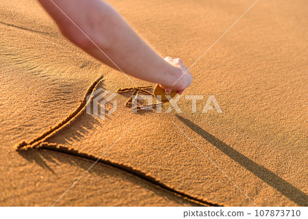 the woman drawing heart shape on sea sand. the woman drawing heart shape on sea sand. 107873710