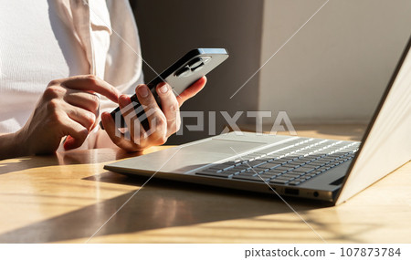 Berlin, Germany October 16 2023 Hand with mobile phone, working at laptop computer. Business communication technologies concept 107873784