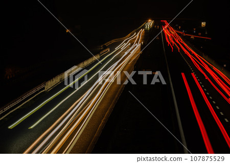 Abstract image of night traffic lights on the road. Car light trails at night in curve asphalt road. Long exposure showing movement of cars 107875529