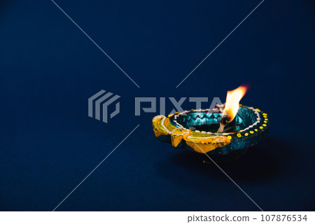 Diwali celebration with vibrant clay diya lamps on a blue background. festive invitations, radiates happiness and prosperity. Shiny glowing lamps. Diwali, Holi, lamp, and god-themed. 107876534