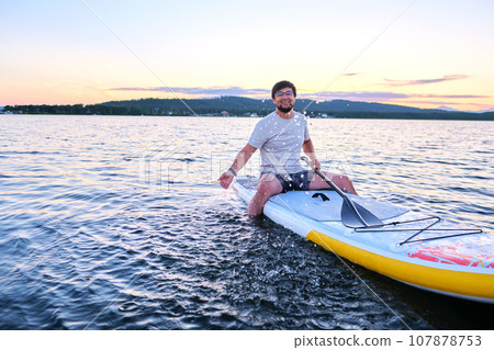 A man sits on a paddle board at sunset. A man sits on a paddle board at sunset. 107878753