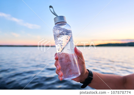A man holds a bottle of water against the backdrop of a lake. 107878774
