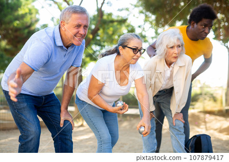 Positive multiracial mature people playing petanque game outdoors in autumn 107879417