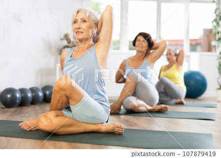 Senior lady performs cow head pose, Gomukhasana 107879419
