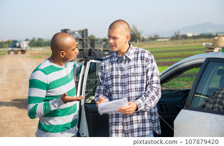 Farmers with papers talking near car on farm field 107879420