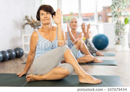 Focused senior women performs Lord of Fishes asana by Ardha Matsyendrasana Focused senior women performs Lord of Fishes asana by Ardha Matsyendrasana 107879434