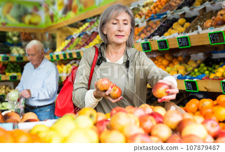 Mature lady choosing fresh apples in greengrocer 107879487