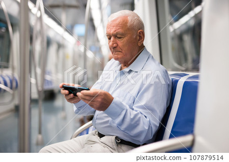 Old man with smartphone sitting inside subway train 107879514