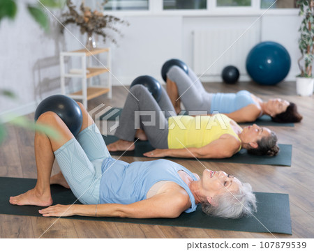 Group of elderly woman doing pilates with soft ball in studio Group of elderly woman doing pilates with soft ball in studio 107879539