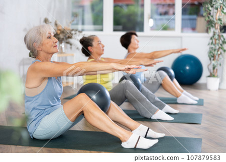 Group of elderly woman doing pilates with soft ball in studio Group of elderly woman doing pilates with soft ball in studio 107879583