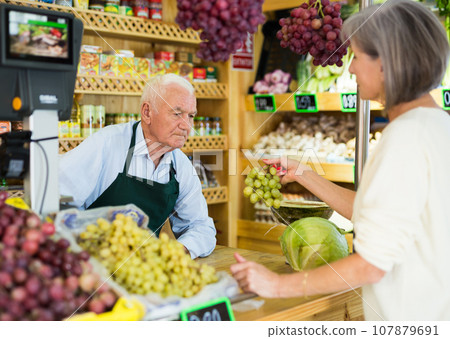 Senior salesman serving woman customer in greengrocer 107879691