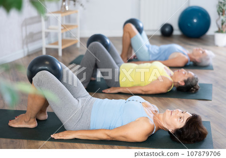 Group of elderly woman doing pilates with soft ball in studio Group of elderly woman doing pilates with soft ball in studio 107879706