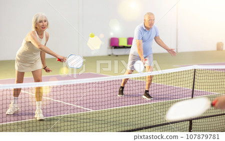 Athletic seniors playing pickleball on court indoors 107879781