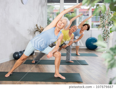 Old woman practicing extended side angle pose of yoga in training room during fitness classes 107879887