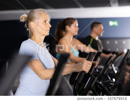 Mature woman exercising on an elliptical trainer in gym 107879918