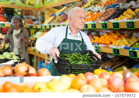 Male supermarket worker carries box of green chili peppers 107879972
