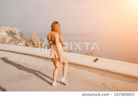 Woman summer dance. Silhouette of a happy woman who dances, spins and raises her hands to the sky. A playful young woman enjoys her happy moment dancing in the rays of the golden sun. 107880605