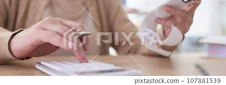 Mature woman makes counts from paper check using calculator 107881539