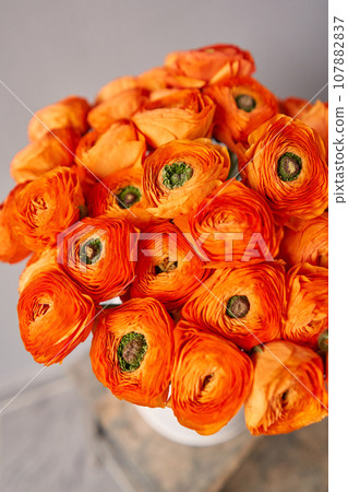 Persian buttercup. Bunch of orange ranunculus flowers on light gray background. Vase on vintage wooden table. Spring background, flower Wallpaper. 107882837