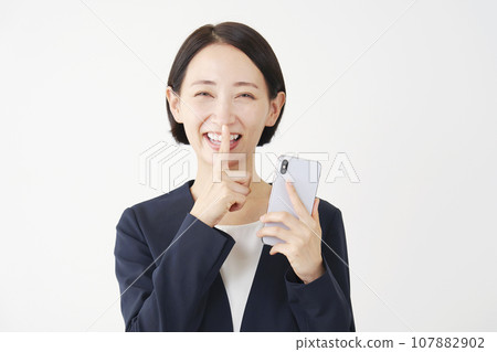 Business woman holding a smartphone and posing secretly, white background Business woman holding a smartphone and posing secretly, white background 107882902