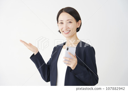 手持智能手機並用手掌白色背景指向左側的女商人 107882942