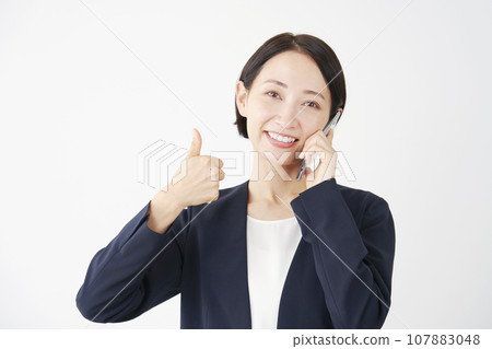 Business woman giving a good sign while calling on a smartphone, white background 107883048