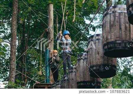 well equipped teenage boys in outdoor passing obstacle course. Active recreation in high rope park 107883621