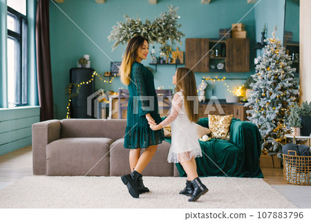 Mother and daughter holding hands in the living room of the house, decorated for Christmas 107883796
