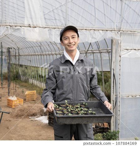 A man with a plastic greenhouse and a box containing seedlings 107884169