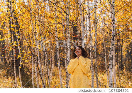 A girl smiles in a yellow knitted sweater in front of the forest A girl smiles in a yellow knitted sweater in front of the forest 107884801