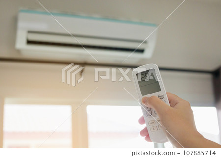Hand with remote control directed on air conditioner inside the room 107885714