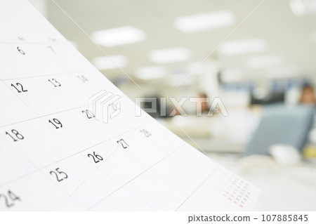 Close up white paper desk calendar on table with blurred office interior background Close up white paper desk calendar on table with blurred office interior background 107885845
