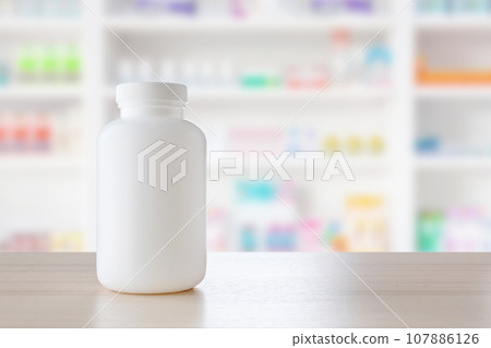 White medicine bottle on wood counter with pharmacy drugstore shelves blur pharmaceutical background 107886126