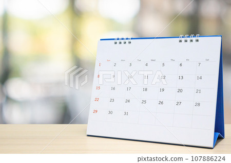 white paper desk calendar on wood table with blurred bokeh background appointment and business meeting concept 107886224