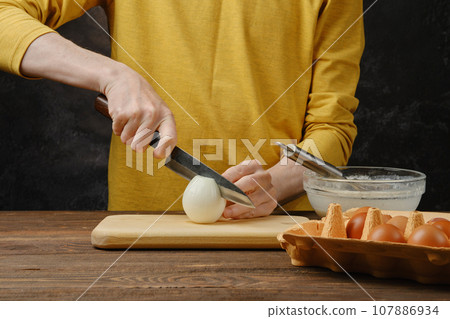 Male hand halving white onion bulb Male hand halving white onion bulb 107886934