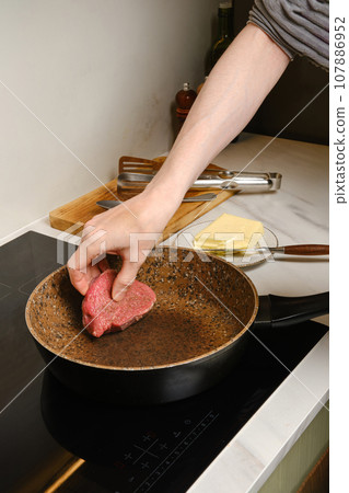 Man put beef steak on frying pan 107886952